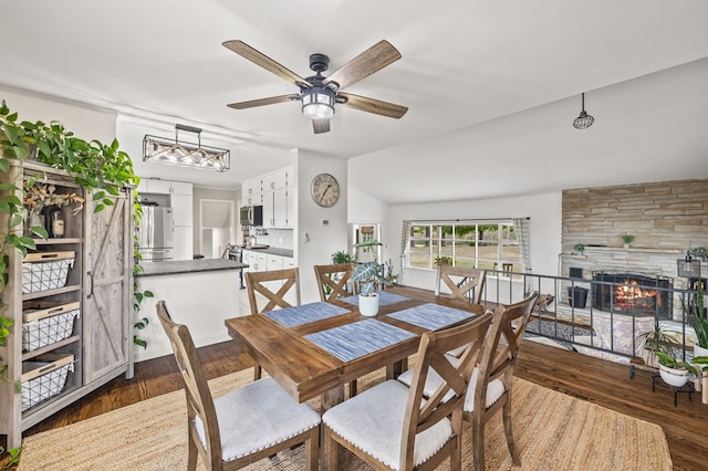 dining room featuring dark wood-style floors, a fireplace, lofted ceiling, and a ceiling fan