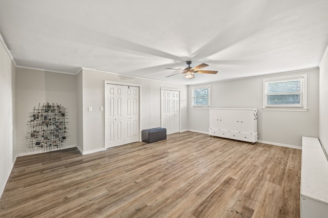 unfurnished bedroom with crown molding, baseboards, two closets, and wood finished floors