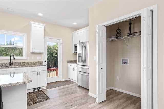 kitchen featuring stainless steel appliances, light stone counters, a sink, and white cabinetry