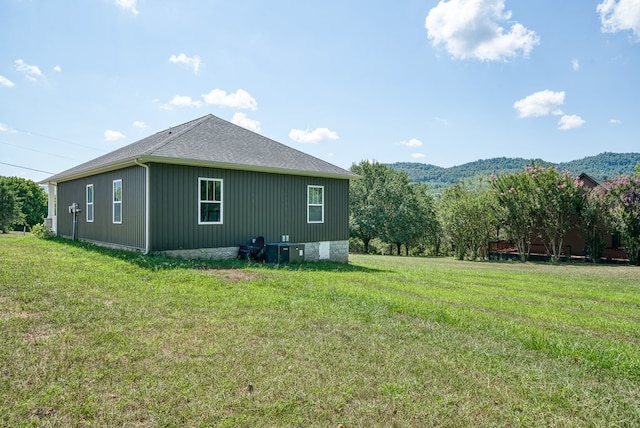 view of side of home with a yard, a shingled roof, and a mountain view