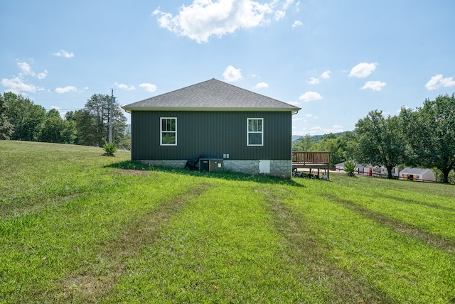 rear view of property featuring roof with shingles, a wooden deck, and a yard