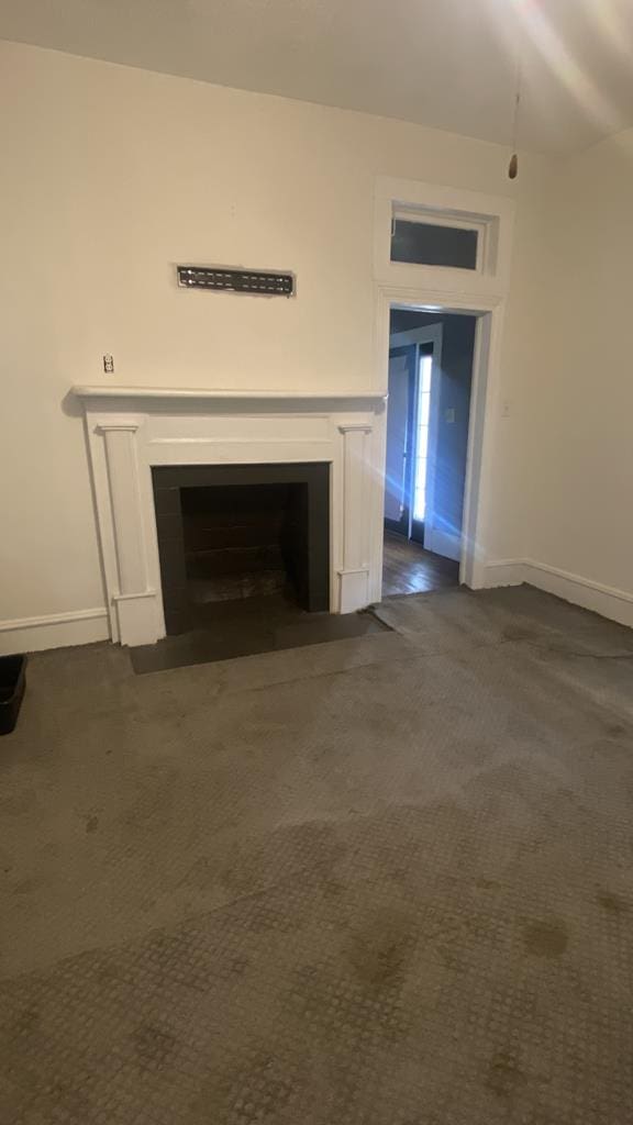 unfurnished living room with a fireplace with flush hearth, dark colored carpet, and baseboards