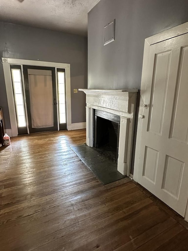 unfurnished living room featuring dark wood-style floors, a fireplace with flush hearth, baseboards, and a textured ceiling