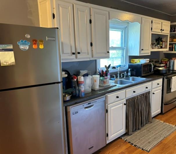 kitchen with white cabinets, dark countertops, light wood-style flooring, stainless steel appliances, and a sink