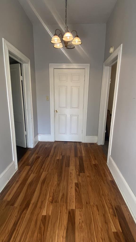 unfurnished dining area with lofted ceiling, an inviting chandelier, baseboards, and dark wood-type flooring