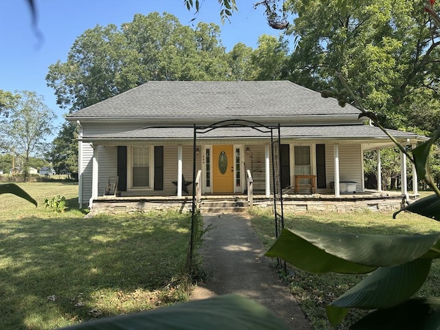 farmhouse-style home with covered porch, roof with shingles, and a front lawn