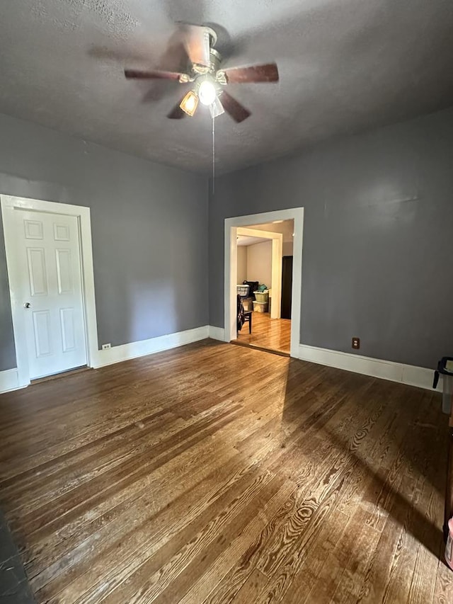 unfurnished bedroom featuring ceiling fan, a textured ceiling, baseboards, and wood finished floors