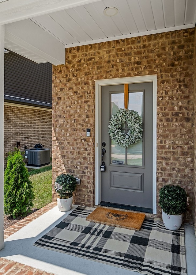 doorway to property featuring brick siding and central AC unit