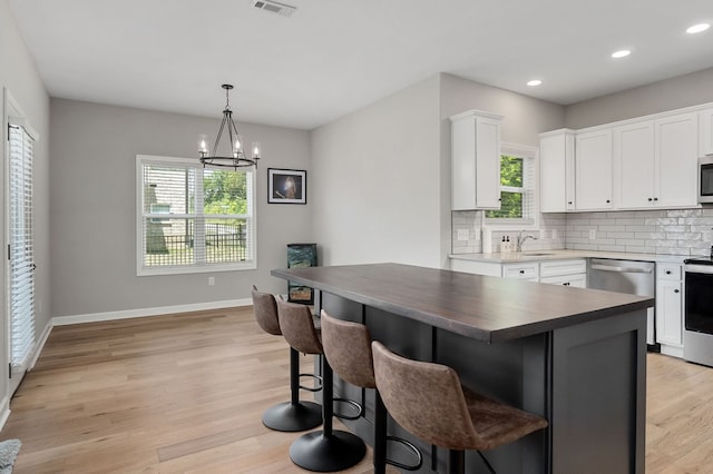 kitchen with decorative backsplash, light wood-style flooring, a kitchen island, white cabinetry, and a sink