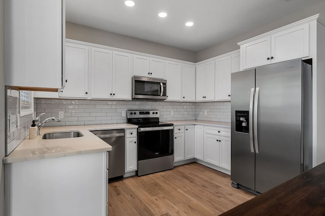 kitchen featuring stainless steel appliances, decorative backsplash, light wood-style floors, white cabinetry, and a sink