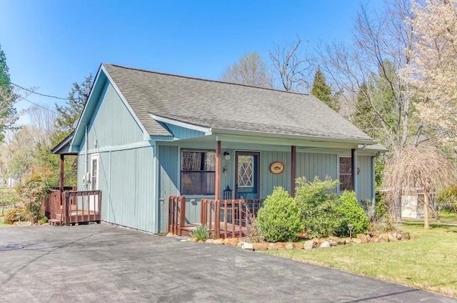 view of front of house featuring a porch, a front yard, roof with shingles, and driveway