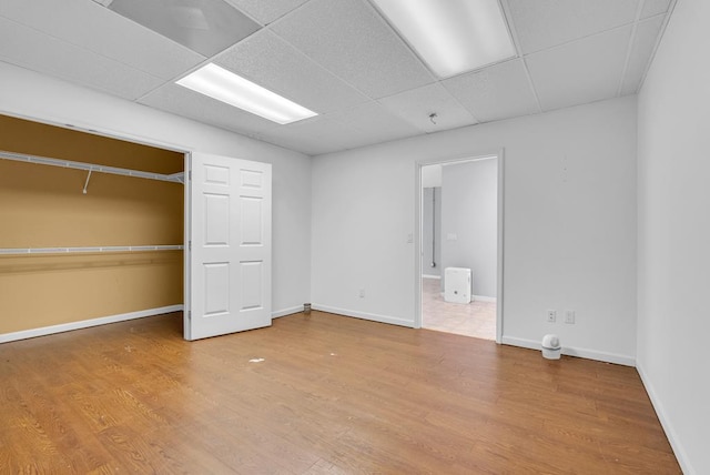 unfurnished bedroom featuring a closet, wood finished floors, a paneled ceiling, and baseboards