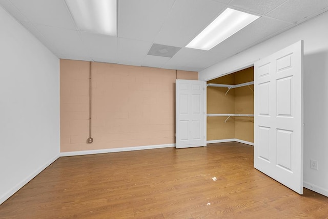 unfurnished bedroom with a drop ceiling, wood finished floors, concrete block wall, and baseboards