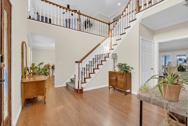 foyer featuring a high ceiling, wood finished floors, baseboards, stairs, and crown molding