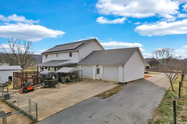 back of property with metal roof, a garage, solar panels, fence, and concrete driveway