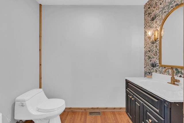 half bath featuring baseboards, wallpapered walls, toilet, and wood finished floors