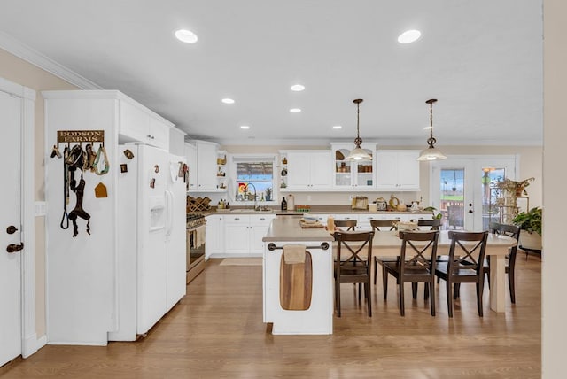 kitchen featuring white refrigerator with ice dispenser, ornamental molding, stainless steel range with gas stovetop, a center island, and a sink