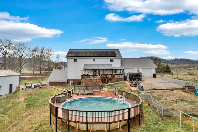 rear view of house with a garage, a wooden deck, solar panels, concrete driveway, and a yard