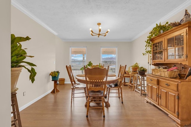 dining room featuring light wood-type flooring, a textured ceiling, a chandelier, and crown molding