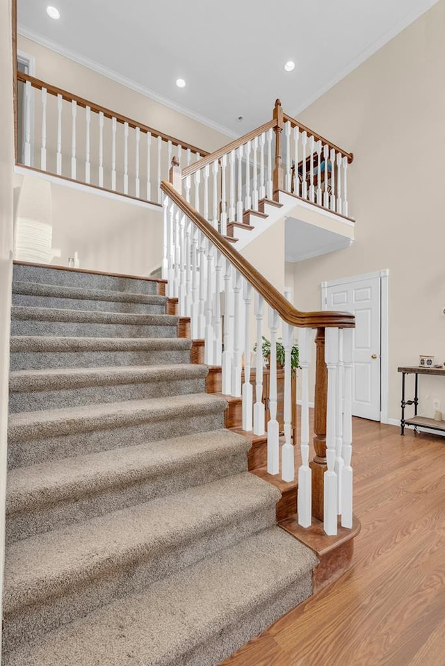 stairs featuring baseboards, a towering ceiling, wood finished floors, crown molding, and recessed lighting