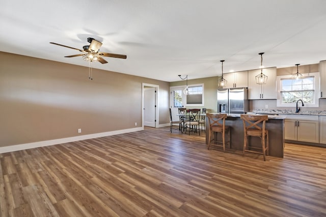 kitchen with a kitchen island, light countertops, stainless steel fridge, a kitchen bar, and decorative light fixtures