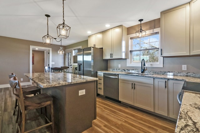 kitchen with stainless steel appliances, hanging light fixtures, a kitchen island, a sink, and light stone countertops