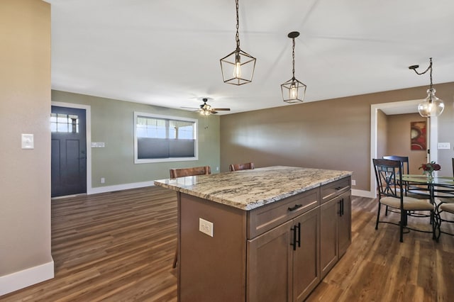 kitchen with dark wood-style flooring, hanging light fixtures, and light stone countertops