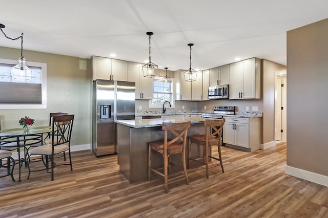 kitchen with dark wood finished floors, a kitchen island, appliances with stainless steel finishes, light stone counters, and a breakfast bar area