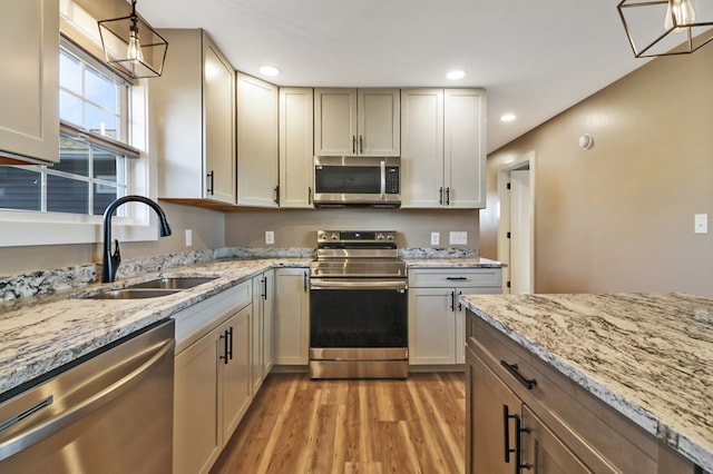 kitchen with light stone counters, light wood-style flooring, recessed lighting, stainless steel appliances, and a sink