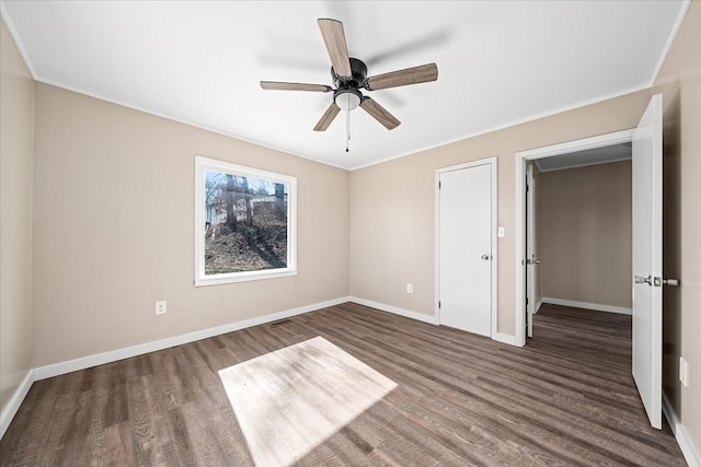 unfurnished bedroom featuring ceiling fan, ornamental molding, dark wood-style flooring, and baseboards