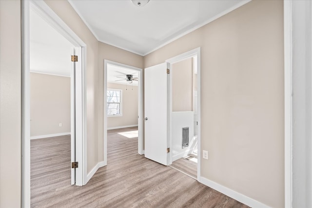 corridor with light wood-type flooring, visible vents, baseboards, and crown molding