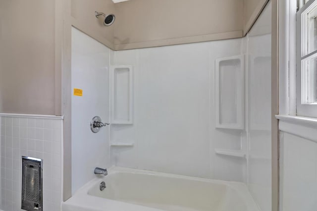 bathroom featuring heating unit, tub / shower combination, tile walls, and wainscoting