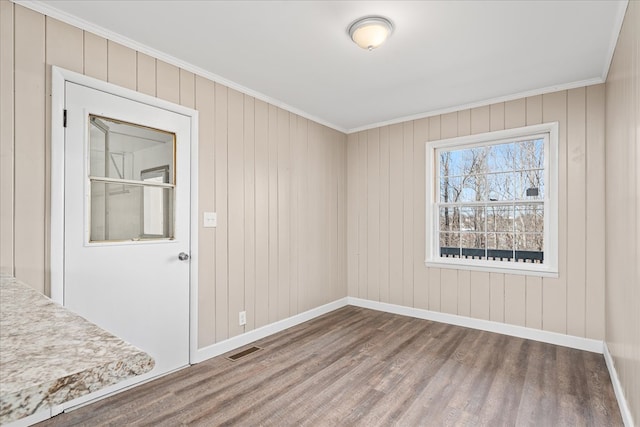 empty room featuring baseboards, wood finished floors, visible vents, and crown molding