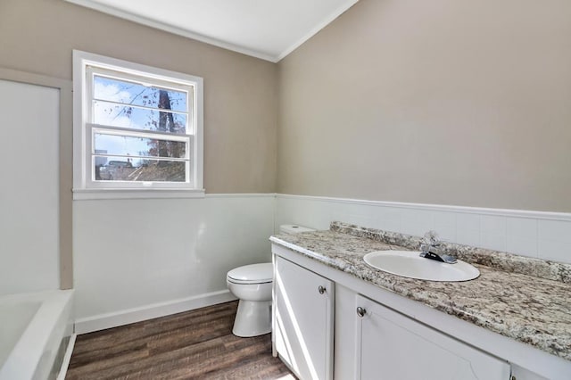 bathroom with a washtub, toilet, vanity, wood finished floors, and baseboards