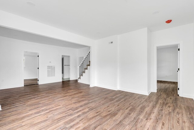 empty room with stairs, wood finished floors, visible vents, and baseboards