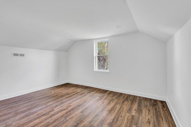 additional living space featuring dark wood-style floors, lofted ceiling, visible vents, and baseboards