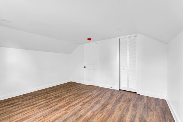 additional living space with dark wood-style floors, baseboards, and vaulted ceiling