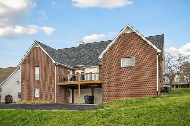 back of property with brick siding, a deck, central AC, and a yard