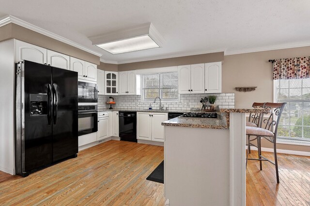 kitchen featuring a peninsula, black appliances, glass insert cabinets, and white cabinets