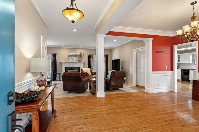 foyer featuring a notable chandelier, wainscoting, light wood-type flooring, ornate columns, and a tile fireplace