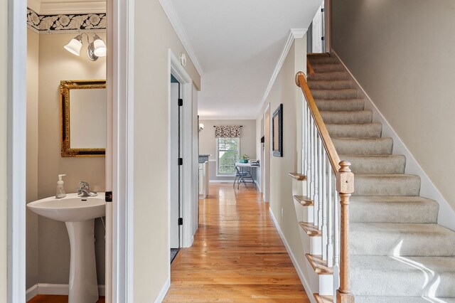 hallway featuring baseboards, light wood-style flooring, stairway, ornamental molding, and a sink