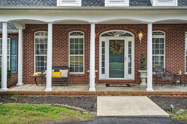 entrance to property featuring covered porch, roof with shingles, and brick siding