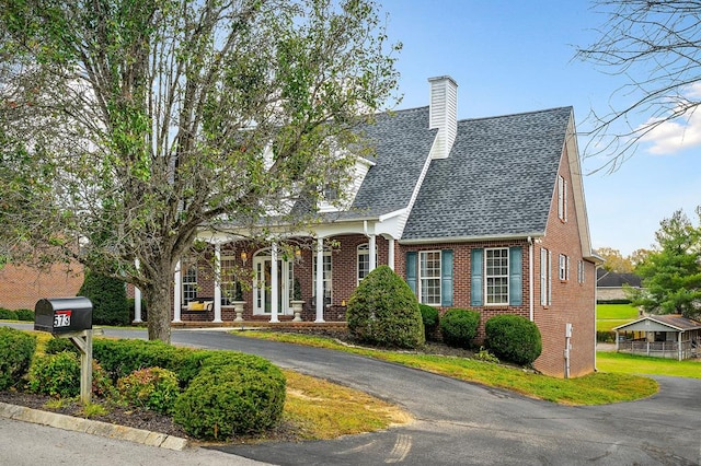 cape cod-style house with driveway, brick siding, a chimney, and a shingled roof