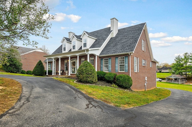 cape cod home with a shingled roof, a chimney, covered porch, a front lawn, and brick siding