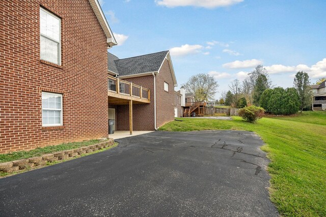 view of side of property featuring stairway, aphalt driveway, a lawn, and brick siding