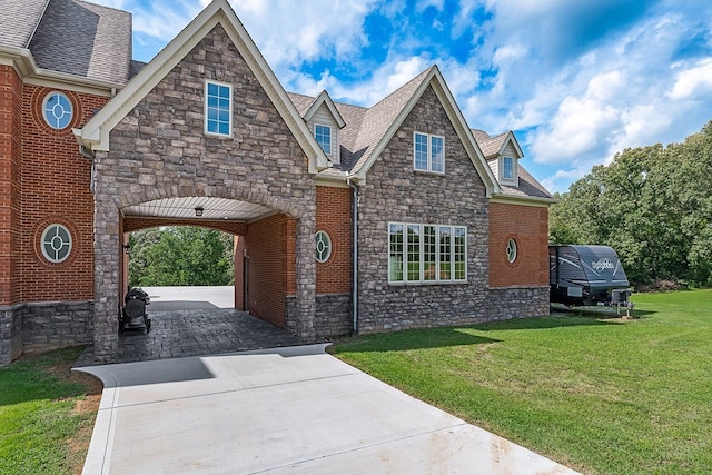 view of front of house with a shingled roof, a front yard, brick siding, and driveway