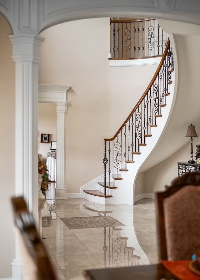 foyer with baseboards, marble finish floor, a towering ceiling, and ornate columns