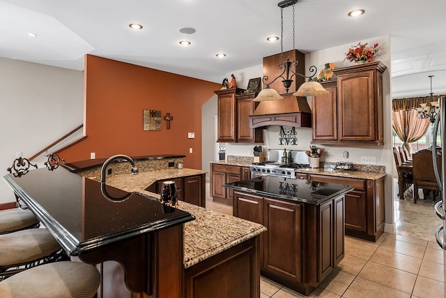 kitchen with dark stone countertops, a center island, decorative light fixtures, stainless steel range oven, and a sink