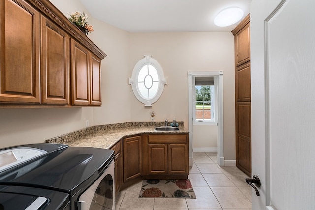 washroom with cabinet space, baseboards, washing machine and clothes dryer, a sink, and light tile patterned flooring