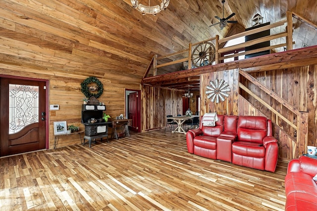 unfurnished living room with wood walls, wood finished floors, high vaulted ceiling, wooden ceiling, and ceiling fan with notable chandelier